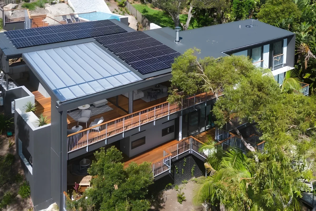 Aerial view of a modern multi-level home with rooftop solar panels surrounded by trees and landscaped outdoor spaces.