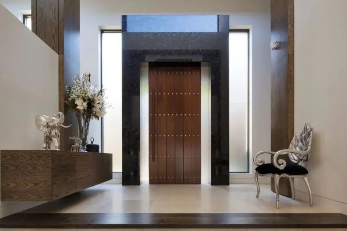 Elegant modern home entryway featuring a large timber front door, high ceilings, custom timber cabinetry, and contemporary interior furnishings.