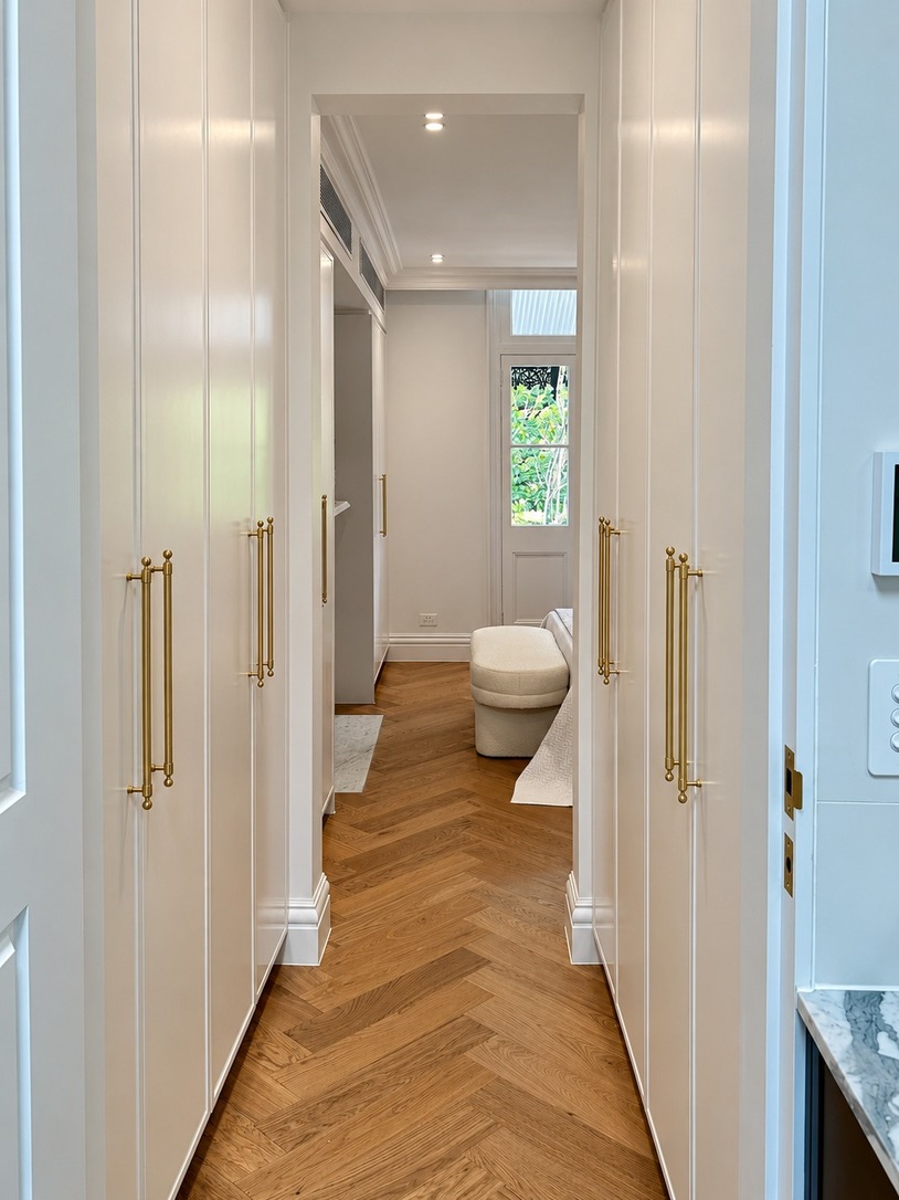 Walk-in robe with brass-handled joinery and herringbone floor leading to the ensuite in a Paddington terrace